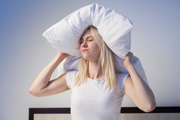 Jeune femme couvrant les oreilles avec un oreiller à cause du bruit.