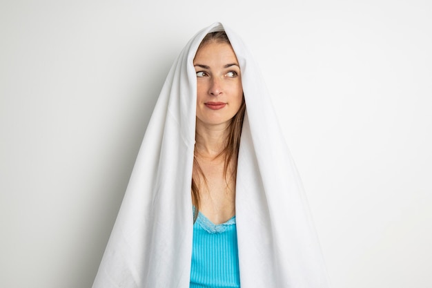 Jeune femme couvrant sa tête avec un drap blanc sur fond blanc