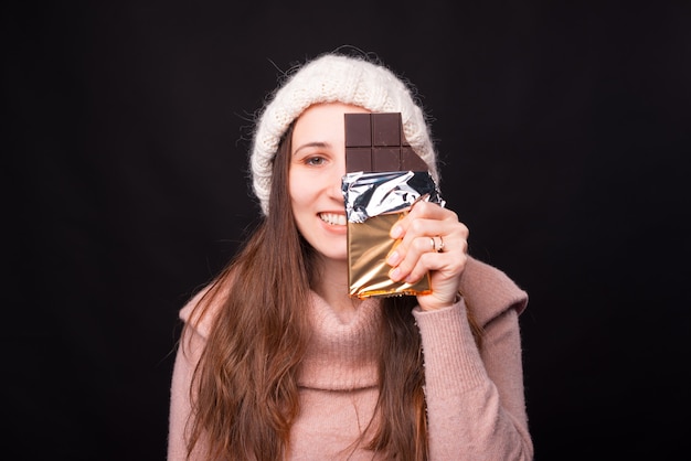 La jeune femme couvre la moitié de son visage avec une barre de chocolat.