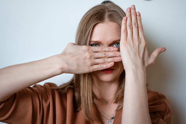 Jeune femme couvre son visage avec ses mains sur le fond d'un mur de lumière