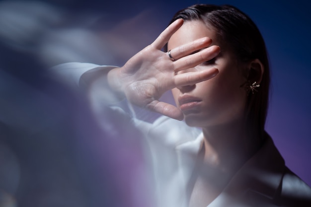 La jeune femme couvre son visage avec ses mains, se cache et dit stop. Jeune femme à la mode élégante en blanc, portrait avec flashs optiques.