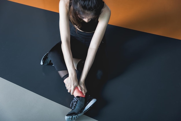 Une jeune femme a une crampe à la cheville lors d'un entraînement physique dans une salle de fitness
