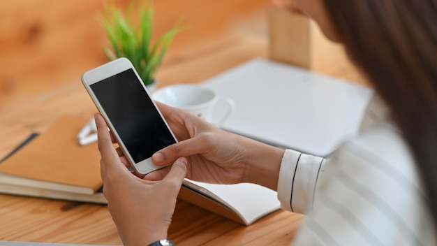 jeune femme créative en merde rayée tout en tenant et en utilisant son smartphone à écran blanc noir au bureau en bois moderne.