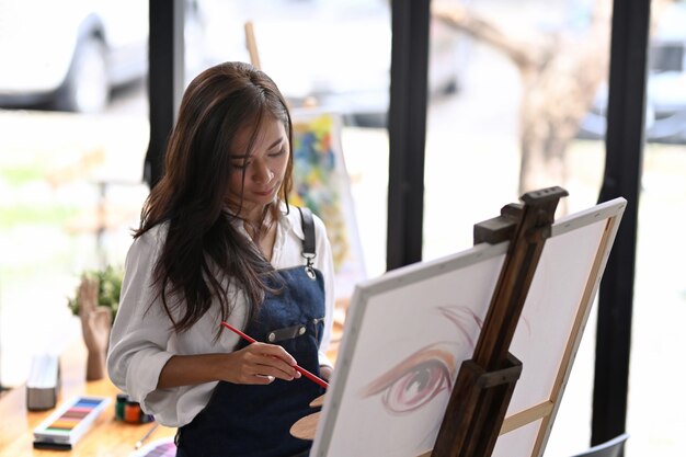 Jeune femme créative peignant sur toile à l'aquarelle dans son atelier.
