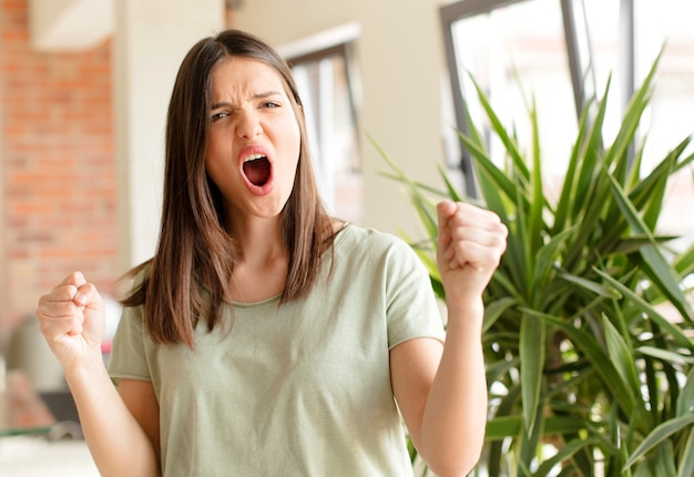 Jeune femme criant agressivement avec une expression de colère ou les poings serrés célébrant le succès