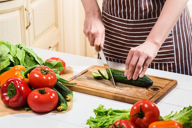 Jeune femme cuisinant dans la cuisine à la maison. Nourriture saine. Diète. Concept de régime. Mode de vie sain. Cuisiner à la maison. Préparer la nourriture. Une femme coupe un concombre et des légumes avec un couteau.