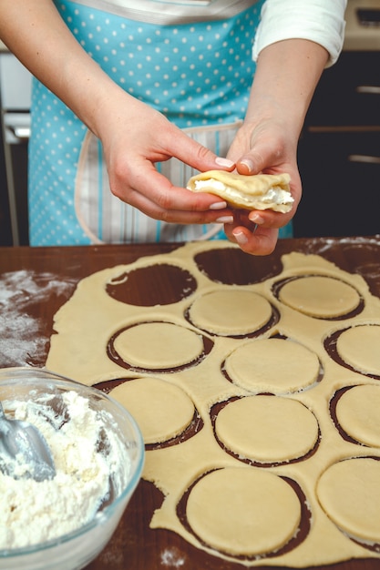 Jeune femme cuisine dans la cuisine, prépare la pâte pour la cuisson, ajoute une farce au fromage cottage en tarte