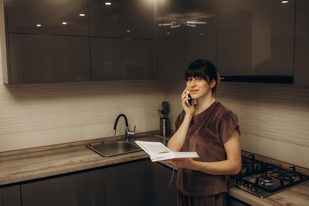 Jeune femme à la cuisine regardant dans un smartphone avec un verre d'eau