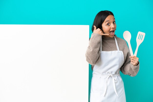 Jeune femme de cuisinier de race mixte avec une grande pancarte isolée sur fond bleu faisant un geste de téléphone et doutant