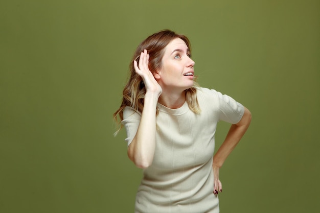 Jeune femme curieuse avec la main près de l'oreille écoutant des potins de rumeur sur le concept de surdité de fond vert