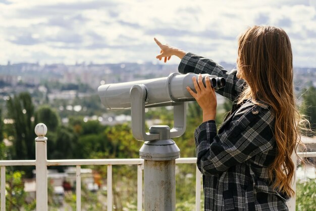 Une jeune femme curieuse pointe du doigt la ville tout en tenant la main sur des jumelles