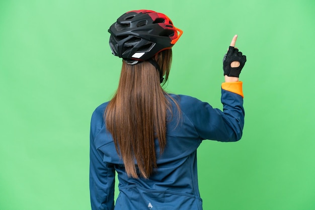 Jeune femme cycliste sur fond isolé chroma key pointant vers l'arrière avec l'index