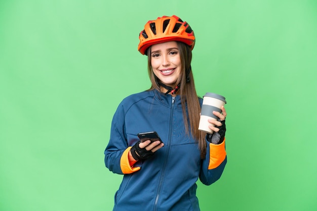 Jeune femme cycliste sur fond isolé chroma key tenant du café à emporter et un mobile