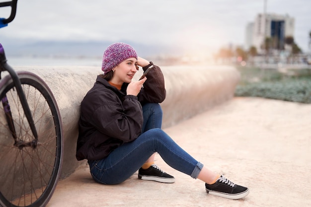 Jeune femme cycliste latine assise seule détendue dans la rue à la plage parlant au téléphone portable