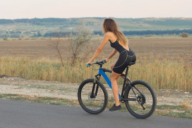 Jeune femme cycliste à vélo sur la vue latérale de la route rurale