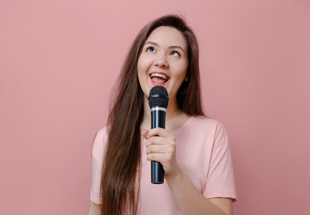 Jeune femme dabbles plisse les yeux avec microphone à la main sur fond rose