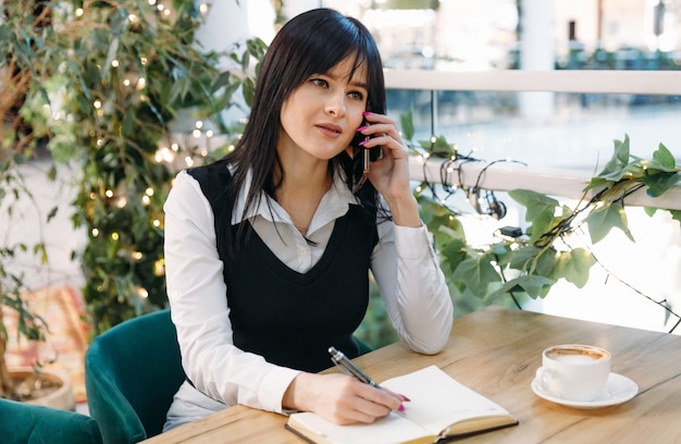 Jeune femme dans un café buvant du café et parlant sur un téléphone portable.