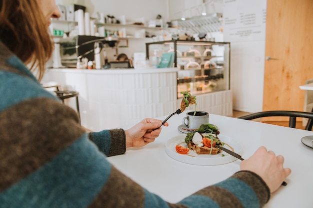 Une jeune femme dans un café mangeant des gaufres végétariennes regardant par-dessus son épaule