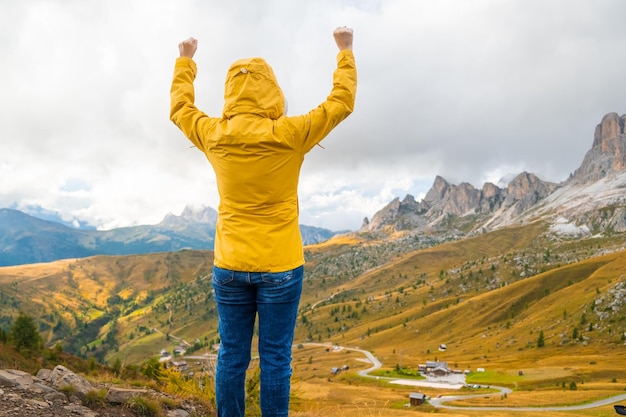 Une jeune femme dans le capot et la veste jaune profitant de la vue sur les montagnes des dolomites italiennes et