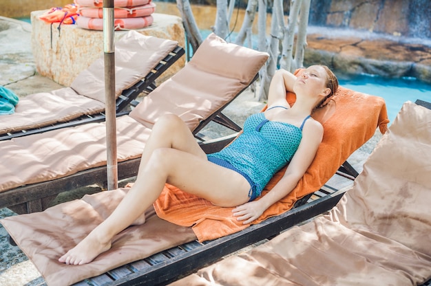 Jeune femme dans une chaise longue au bord de la piscine