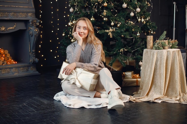 Jeune femme dans un chandail gris assis près de l'arbre de Noël