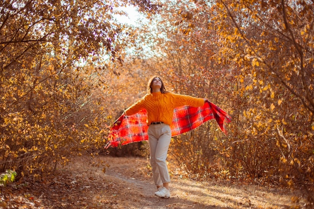 Une jeune femme dans un chandail orange s'enveloppe dans une écharpe dans un parc d'automne