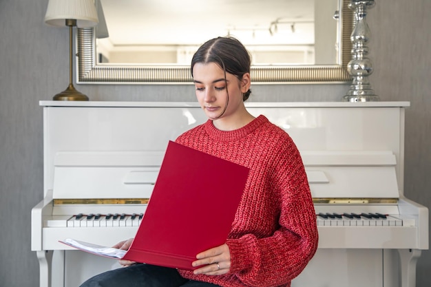 Une Jeune Femme Dans Un Chandail Tricoté Rouge Près D'un Piano Blanc