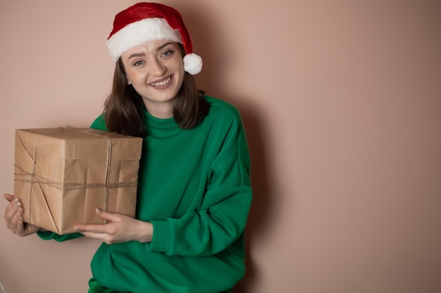 Jeune femme dans un chandail vert et dans un chapeau du Nouvel An tient une boîte-cadeau sur un simple fond vert Concept de vacances Bonne année 2023 clé chrome joyeux noël