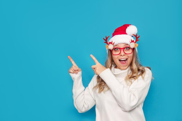 Une jeune femme dans un chapeau de Noël de Noël lunettes drôles pointe sur l'espace de copie pour le texte ou la conception