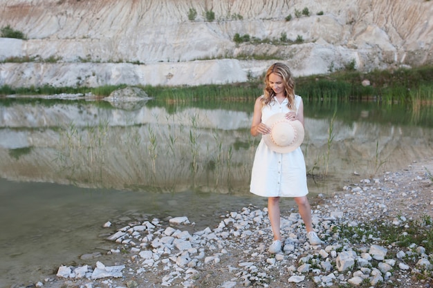 Jeune femme dans un chapeau près d'un lac avec de l'eau légère et des collines de sable.