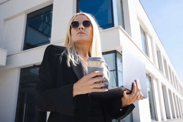 Une jeune femme dans un costume élégant avec un ordinateur portable et une tasse de café sur le fond d'un centre d'affaires