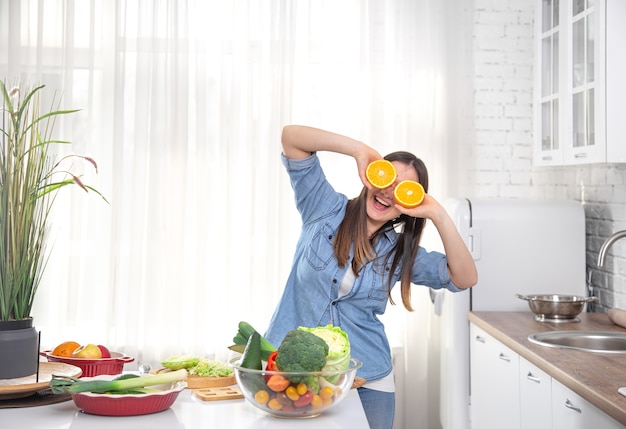 Photo jeune femme dans une cuisine lumineuse posant avec des oranges pendant la cuisson.