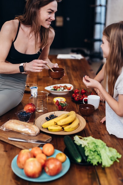 Jeune Femme Dans La Cuisine Mettant De La Nourriture Sur Une Assiette Pour Une Petite Fille.