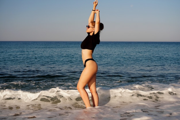 Jeune femme dans un débardeur noir et un caleçon sur la plage de la mer