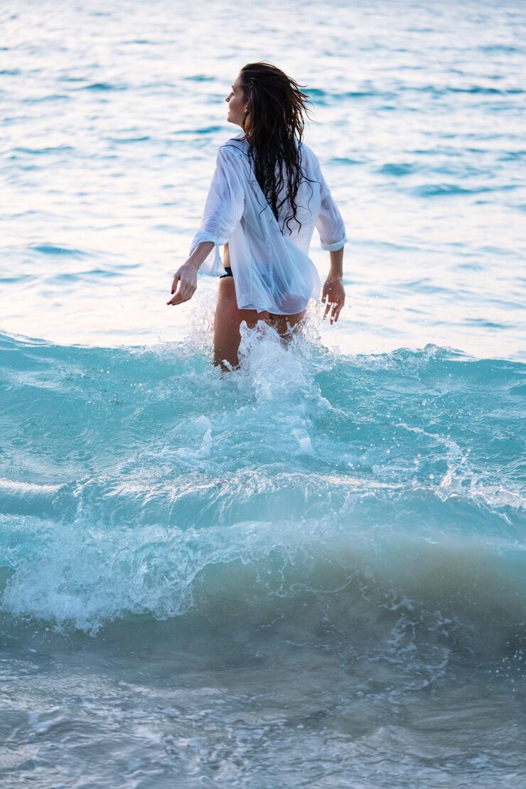 Photo une jeune femme dans l'eau à la plage au coucher du soleil