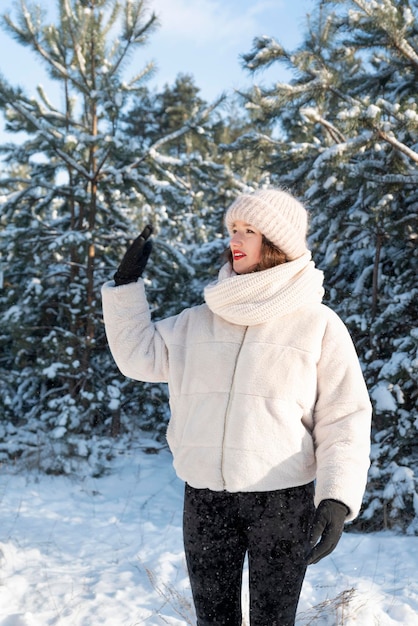 Jeune femme dans la forêt d'hiver agite sa main. Temps ensoleillé en hiver, vacances.