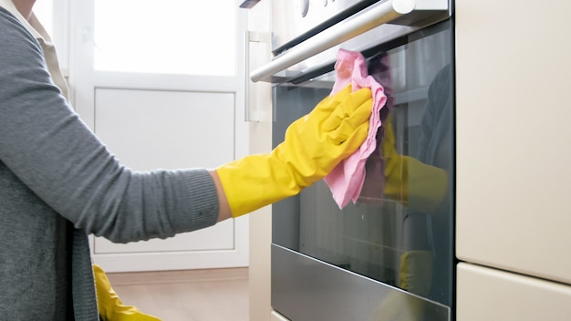 Jeune femme dans des gants en caoutchouc nettoyant la cuisine avec un chiffon et un détergent.