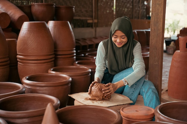 La jeune femme dans un hijab s'assied travaillant l'argile dans la poterie