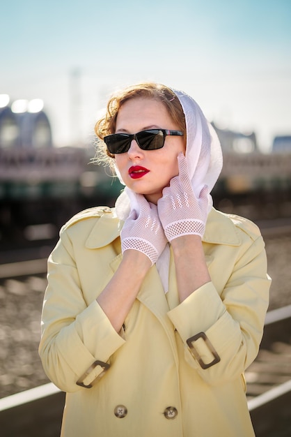 Une jeune femme dans un imperméable jaune avec des lunettes noires sur le quai de la gare