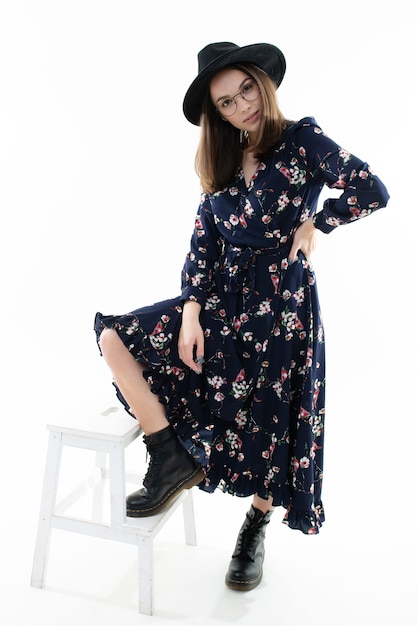 Jeune femme dans une longue robe à fleurs avec un chapeau pose pour la caméra