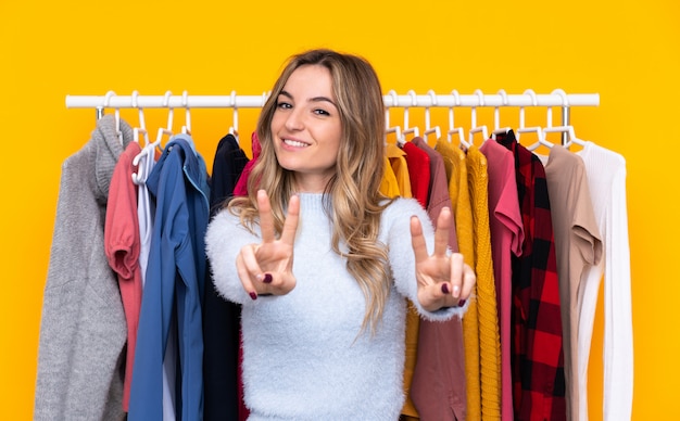 Jeune femme dans un magasin de vêtements souriant et montrant le signe de la victoire