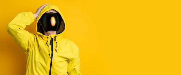 Une jeune femme dans un masque de lunettes cyberpunk dans une veste jaune tient sa tête avec sa main sur un fond jaune Bannière