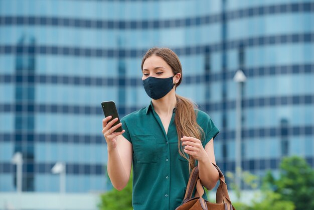 Une jeune femme dans un masque médical bleu marine pour éviter la propagation du coronavirus tenant son sac en cuir