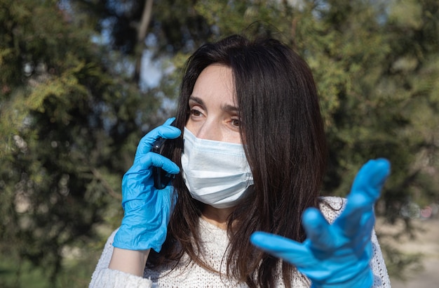 Jeune femme dans un masque médical avec un téléphone portable communique émotionnellement et fait des gestes