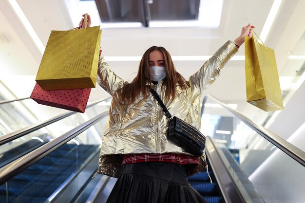 Une jeune femme dans un masque de protection après le shopping monte l'escalator