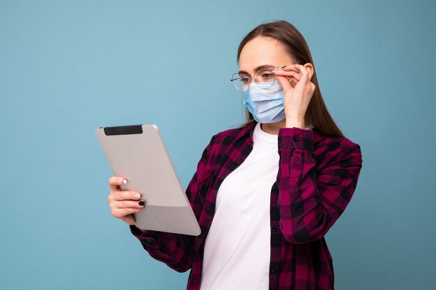Une jeune femme dans un masque de protection types sur une tablette sur un fond bleu