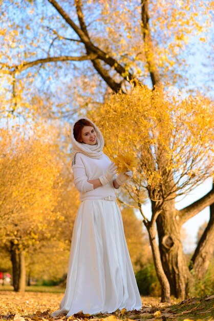 Jeune femme dans un parc en automne. Dame aux feuilles en robe blanche