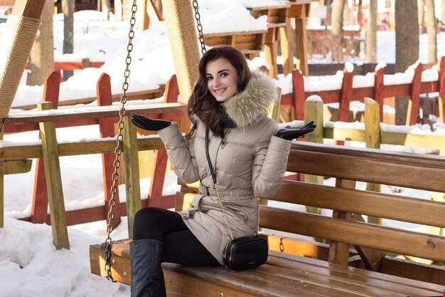 Jeune femme dans le parc d'hiver assis sur un banc avec beaucoup de neige autour