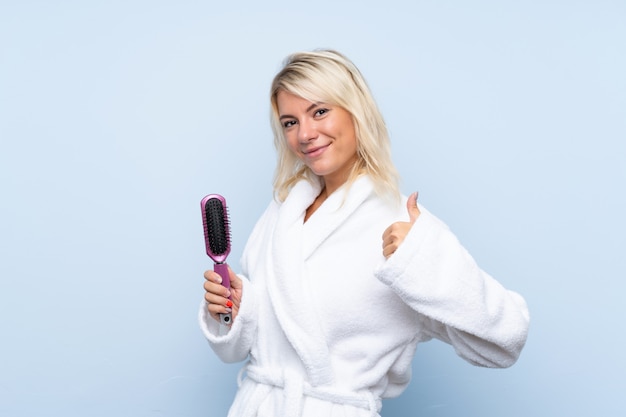 Jeune femme dans un peignoir avec un peigne à cheveux avec le pouce levé parce qu'il s'est passé quelque chose de bien