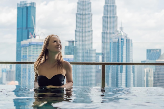 Jeune femme dans la piscine extérieure avec vue sur la ville dans le ciel bleu